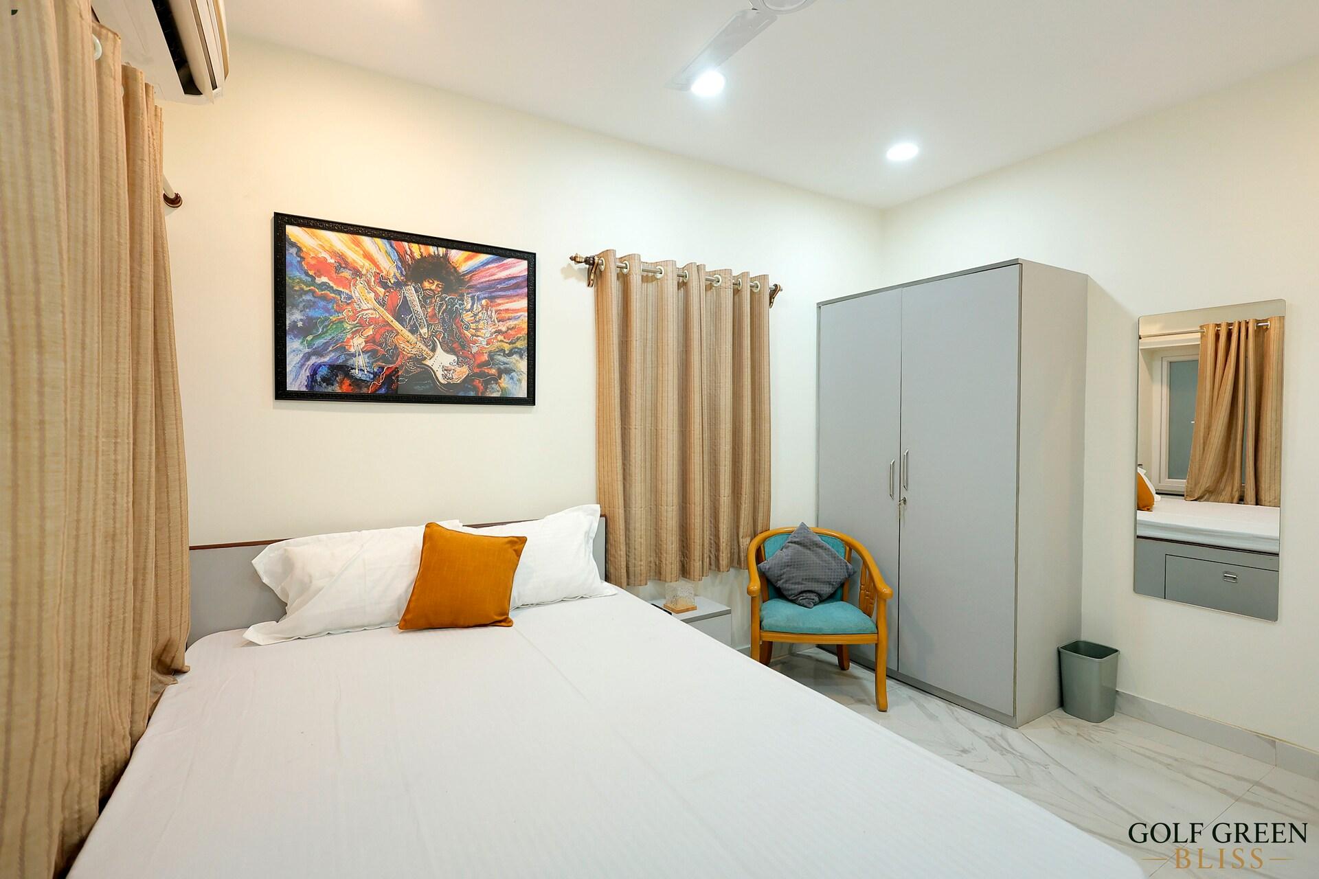 Bedroom one with a queen bed, framed artwork, wardrobe and an armchair beside the curtained window