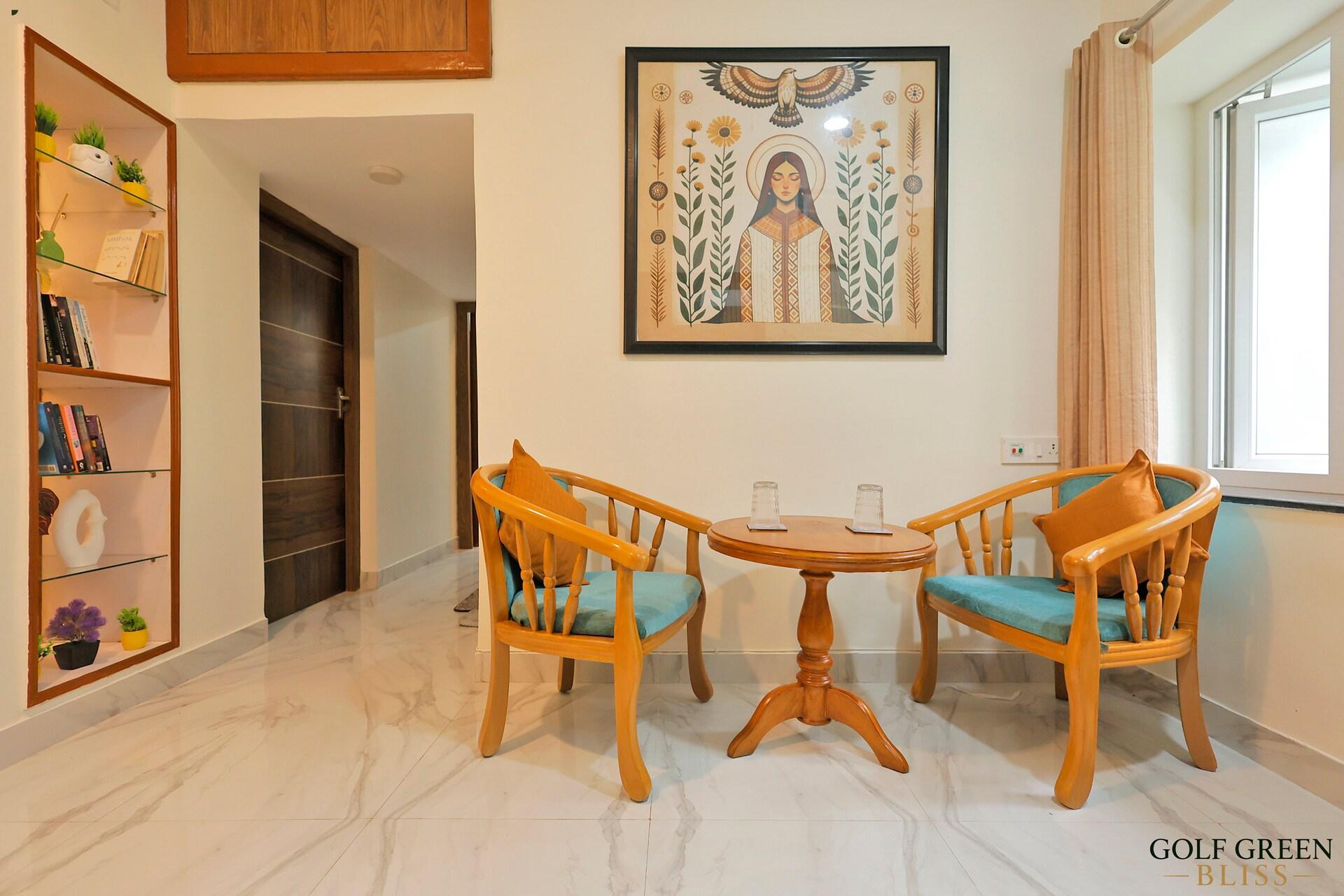 The dining area with a round wooden table and two cushioned armchairs below a framed print